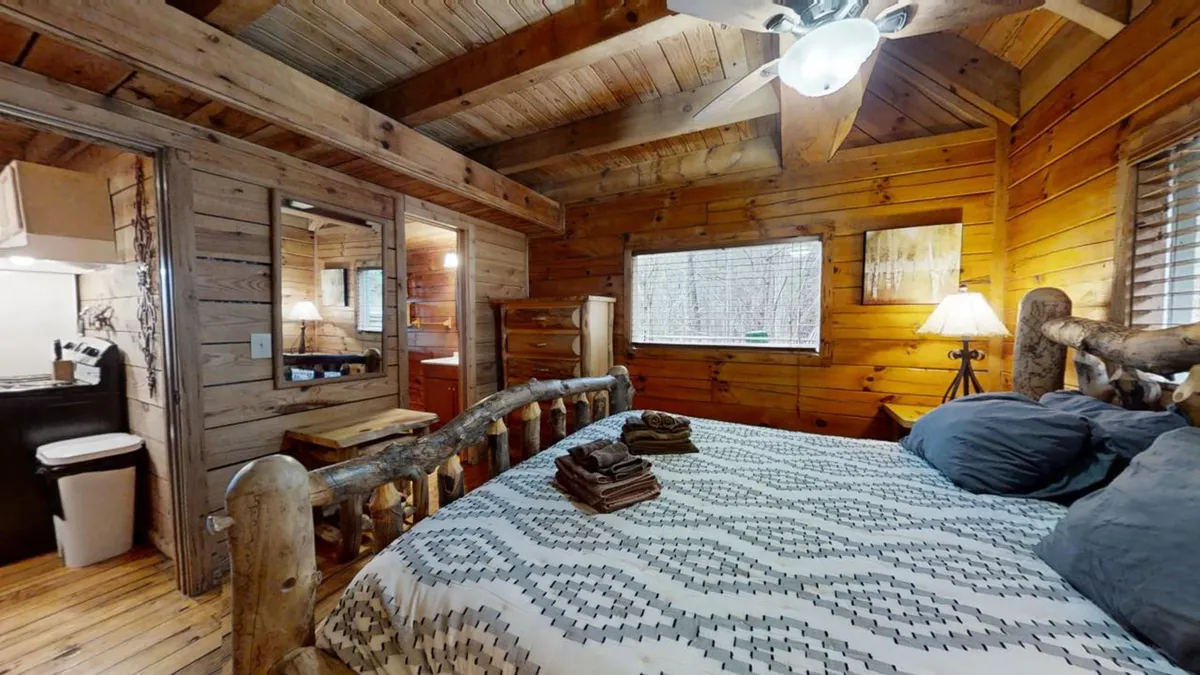 A bright, peaceful bedroom with a wooden bed frame, plush bedding, and a window letting in natural light. Fresh towels are neatly arranged on the bed, and the view through the window hints at the serene mountain environment outside.