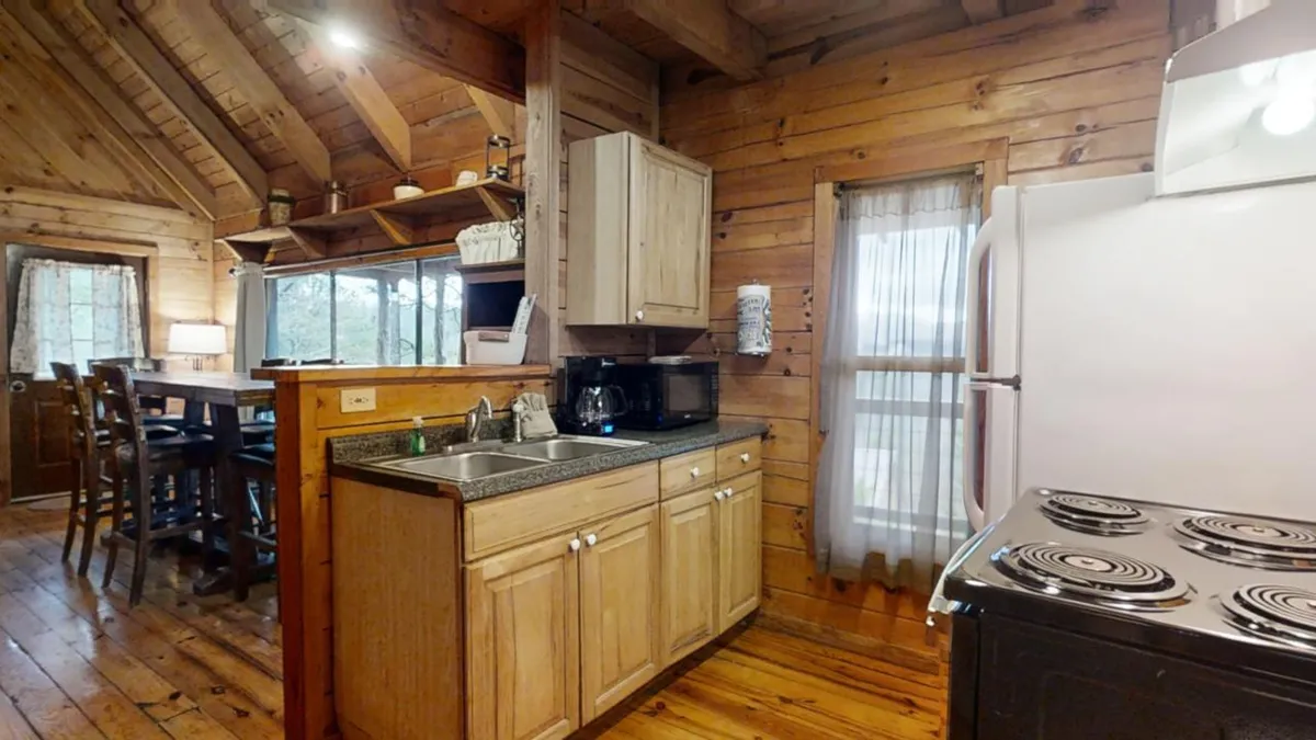 A cozy kitchen scene with wooden cabinets, a kitchen island, a large window providing ample natural light, and a stove. The space feels open for socializing and entertaining, ideal for sharing recipes and enjoying special occasions.
