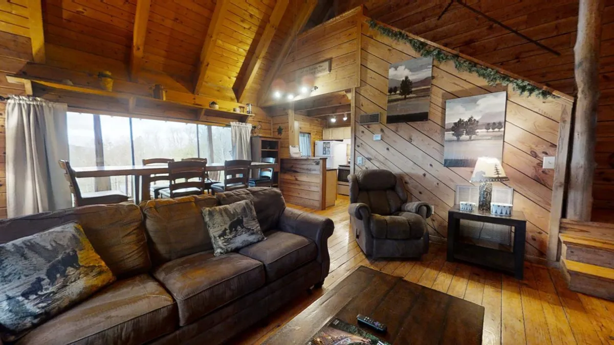 This inviting interior scene shows a cozy living room with a sofa adorned with accent pillows, a dining area perfect for family meals, and warm wooden beams overhead. Artwork on the walls adds a touch of personality, and the arrangement suggests a space for relaxation, socializing, and making memories together.