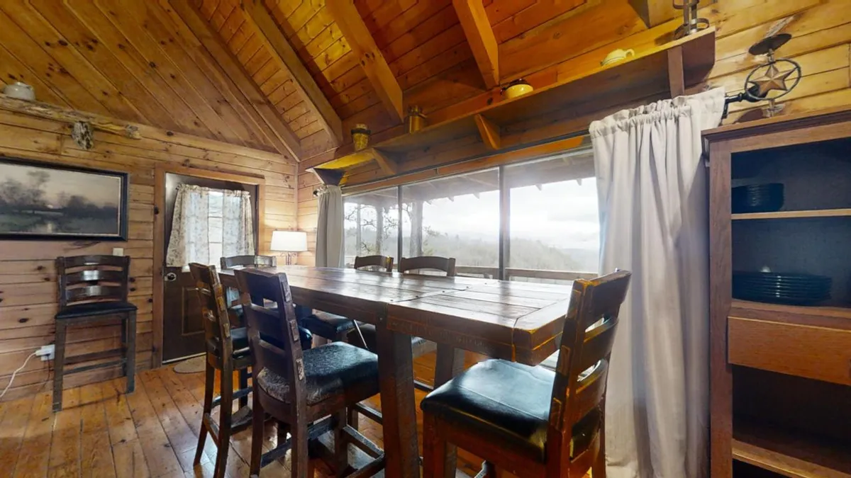A rustic wooden dining table set near large windows that overlook scenic views. The room features decorative shelves and beams, creating a cozy spot for family meals, game nights, and memorable gatherings.