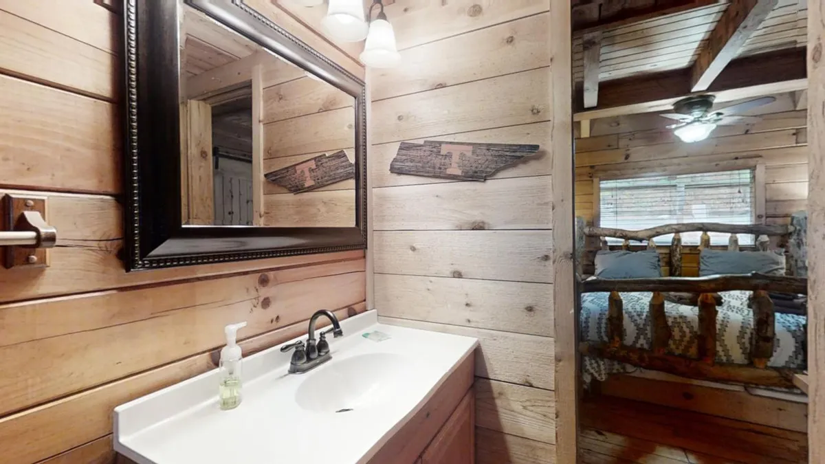 A rustic vanity area with a large mirror, wooden accents, and a glimpse of a comfortable bed in the background, all softly illuminated. The decor and layout provide a sense of relaxation and personal retreat.