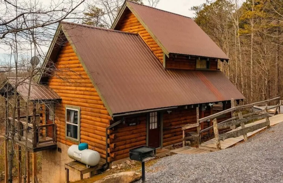 This exterior shot captures the log cabin's rustic charm, wooden railing, and lush surroundings. The porch invites gatherings, barbecues, or simply unwinding after a day of adventure. The natural setting underscores the cabin's connection to the outdoors and the opportunities for pet-friendly fun and family activities.