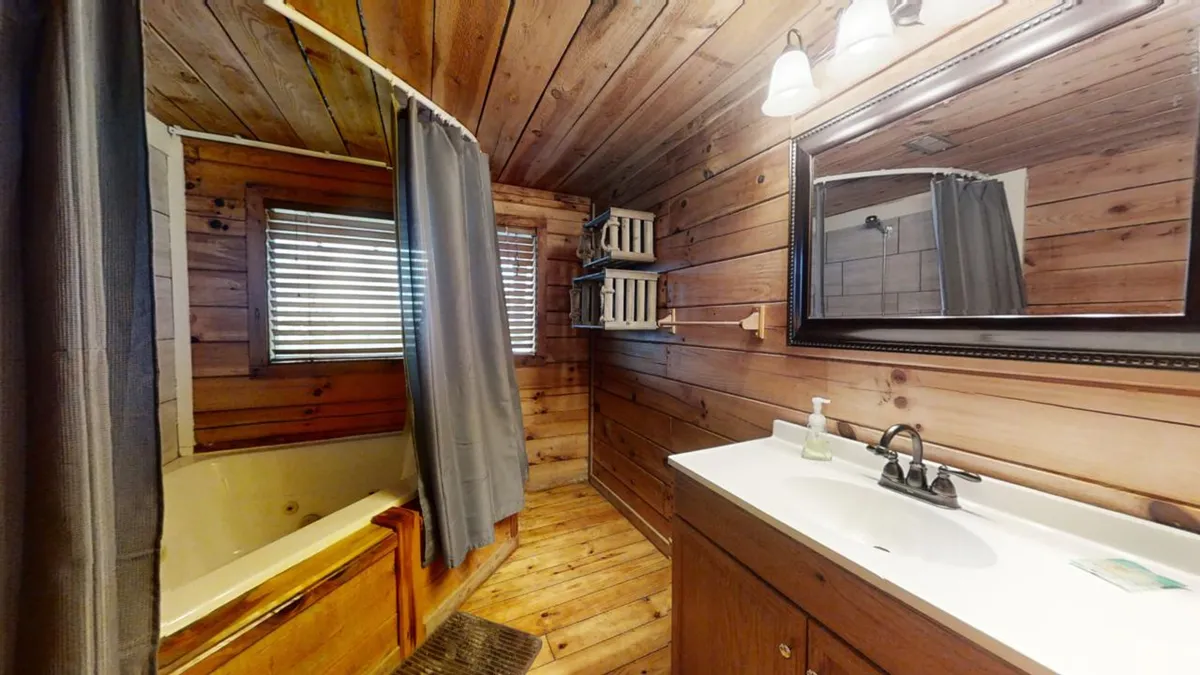 A tranquil bathroom with a luxurious bathtub set against wood-paneled walls, a sink with a mirror, and a window letting in soft daylight. The space feels private, spa-like, and inviting—ideal for unwinding after a long day.