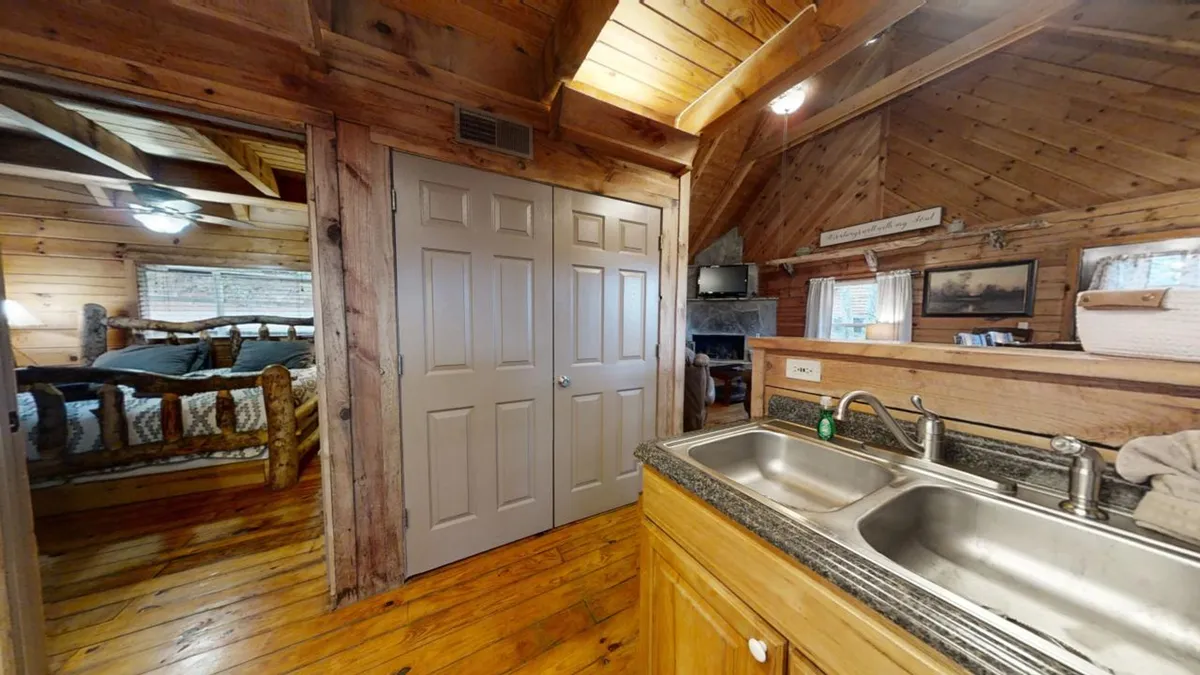 A welcoming kitchen scene featuring a farmhouse-style sink, wooden cabinets, and a doorway that leads into a softly lit bedroom. The inviting space suggests morning coffee rituals and shared meals, emphasizing the comfort and homey feel of the cabin.